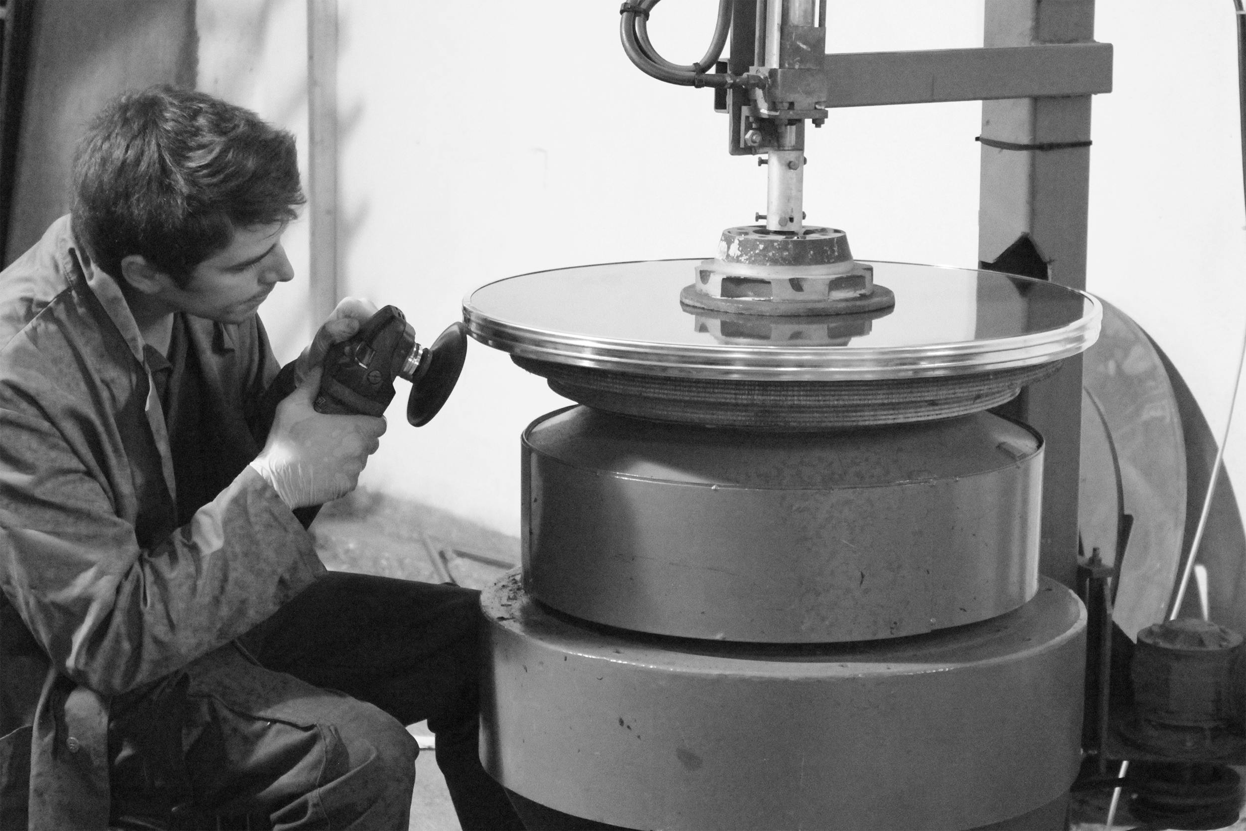 A concentrated worker polishes a large metal disc in an industrial setting.