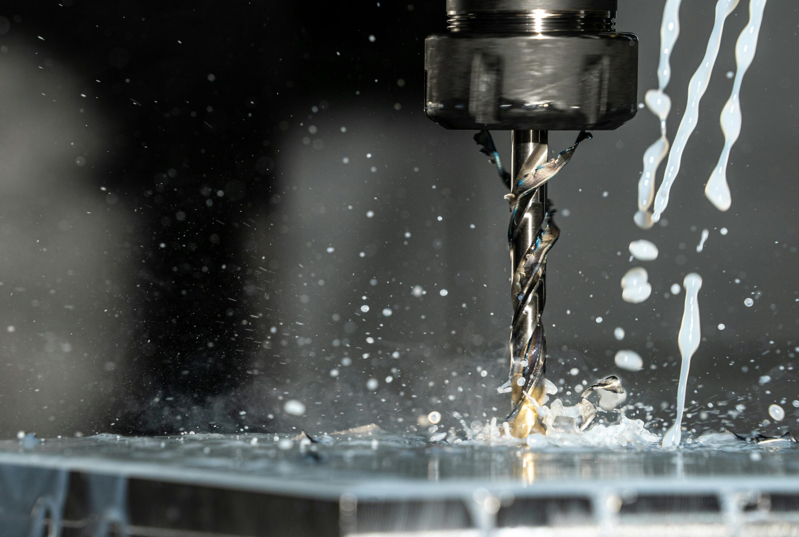 High-speed close-up of CNC drill bit in action with water splash for lubrication.